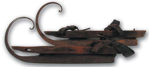 Late ninteenth-century wood and metal skates with an elaborate upward curl at the front of the blade. 